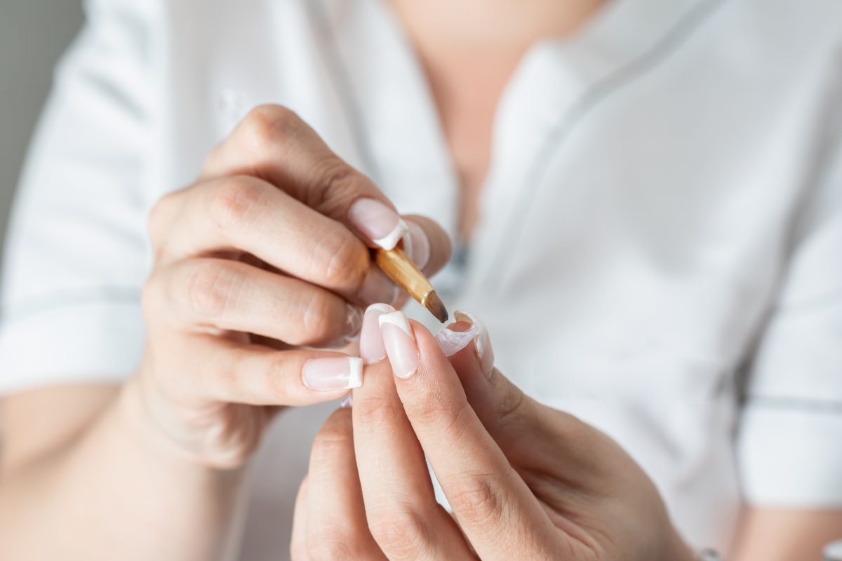 latin woman specialist in manicure, using the brush to correctly spread the liquid gel on the artificial nail, to later place it on the nails and make a polygel. beauty concept