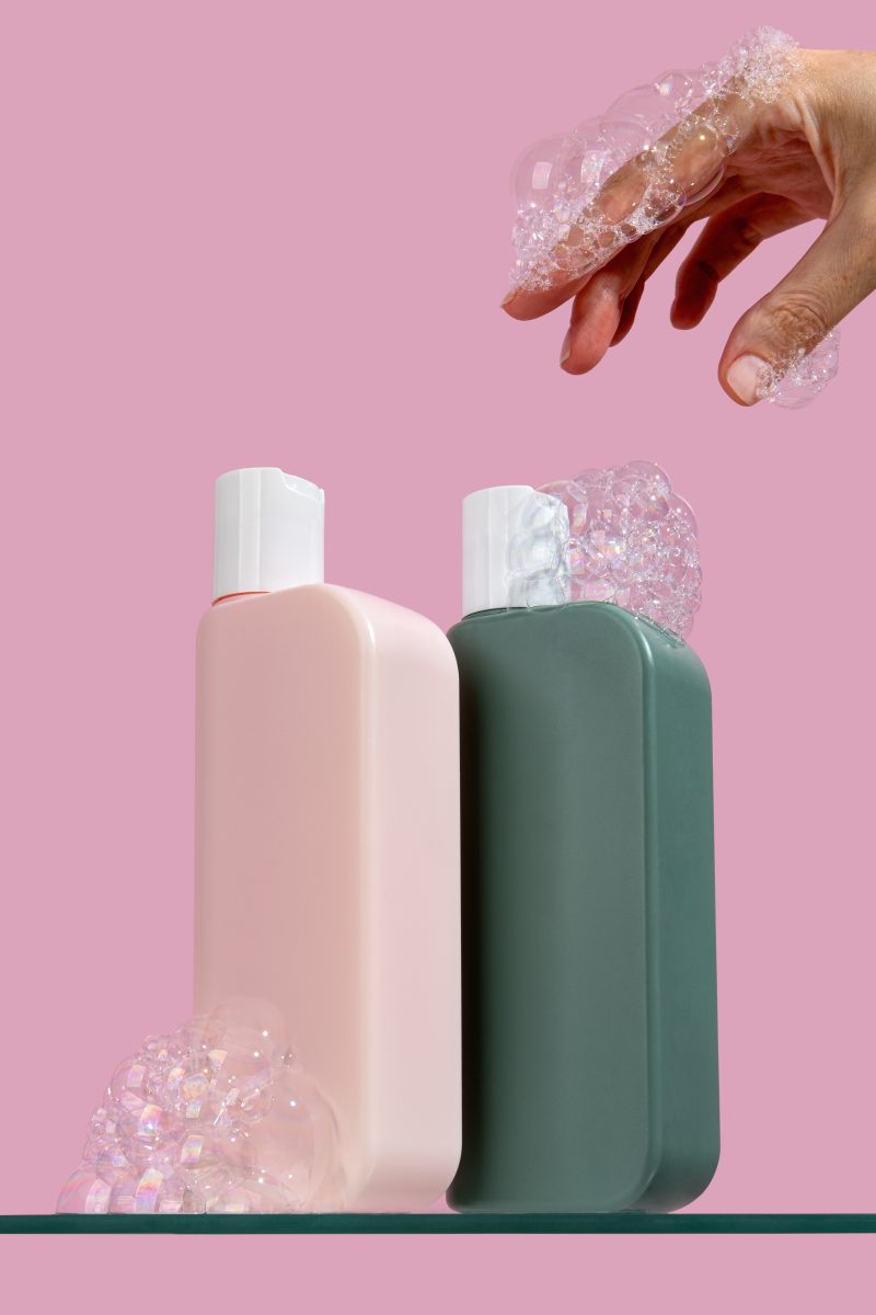 Two tubes of shampoo and hair conditioner packaging stand on a glass shelf on light pink background. Set of accessories for hygiene. Natural organic spa cosmetic concept, minimalism brand packaging mock up. The Case for Sulfate-Free Formulas