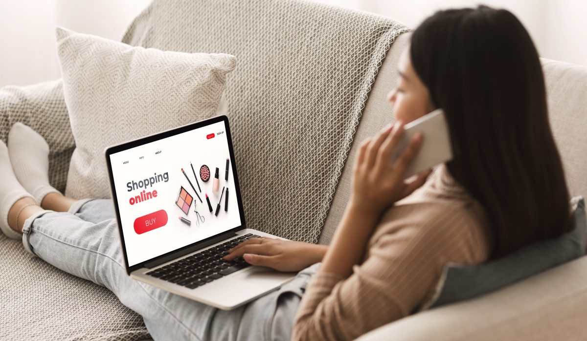 Female Shopping Concept. Back view of woman browsing online make up store, talking on phone, sitting at home