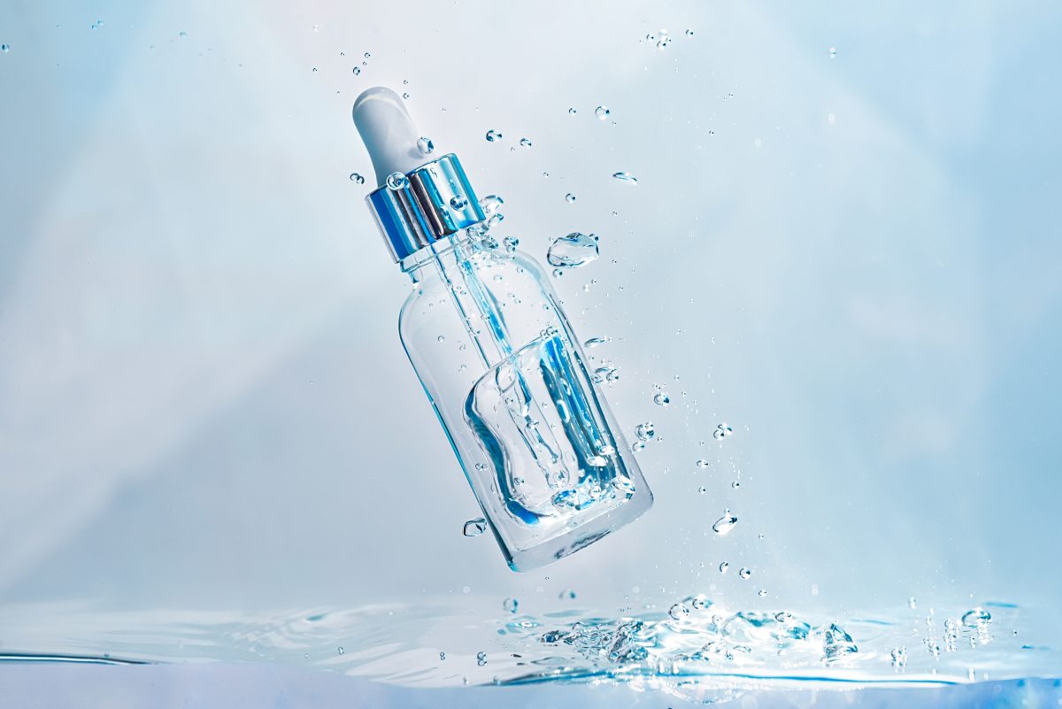 Cosmetic essence in a glass bottle with a pipette in a transparent liquid, water with bubbles. Concept of natural Hydration cosmetics, skin care serum. Scientific developments of modern cosmetics. What Is Hyaluronic Acid and How Does It Work on a Cellular Level