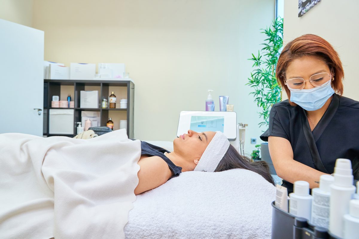 Esthetician preparing them to do a facial cleansing of a woman's skin.