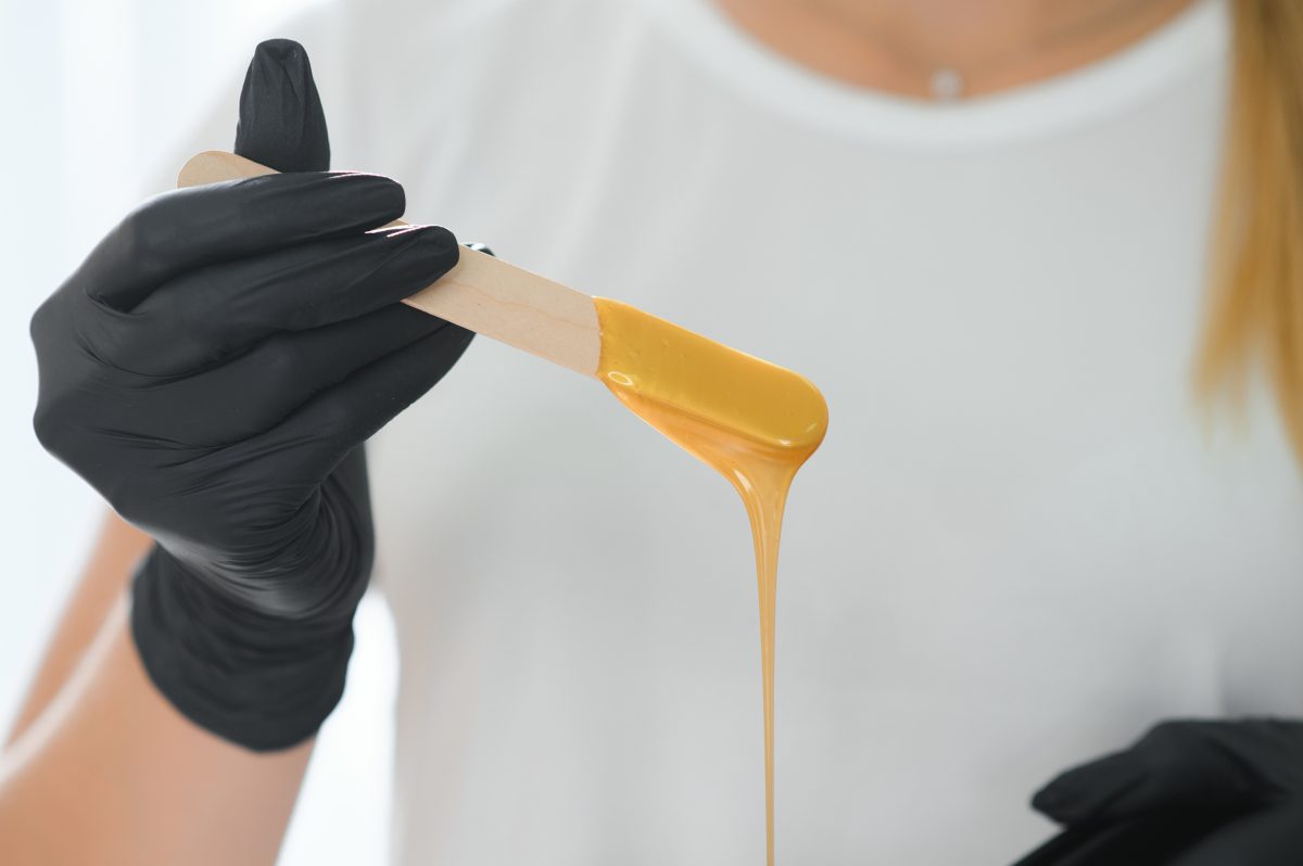 Female cosmetologist holding stick with wax for depilation or sugaring.