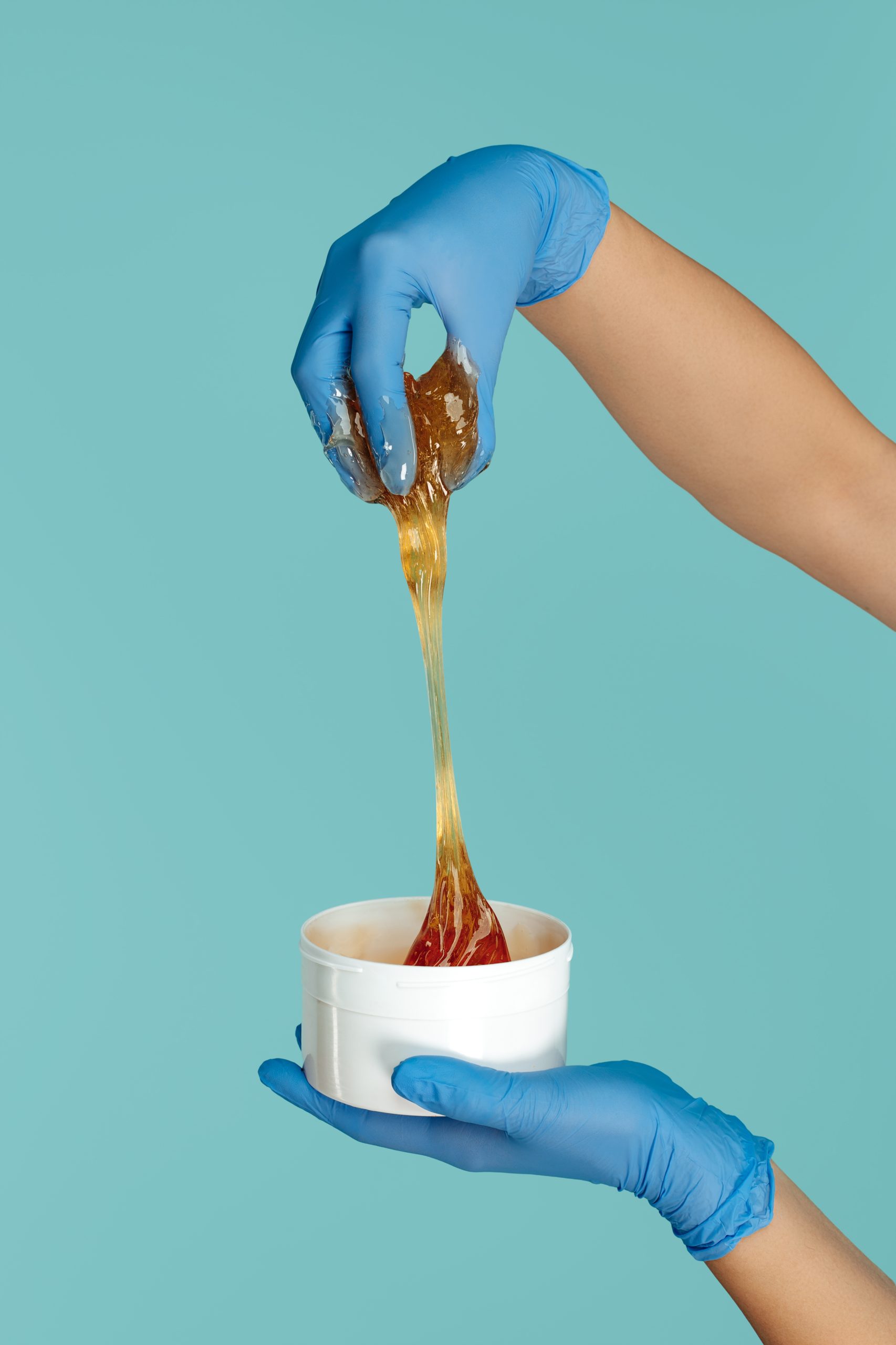 Hands holding bucket with sugaring paste for depilation procedure over blue background