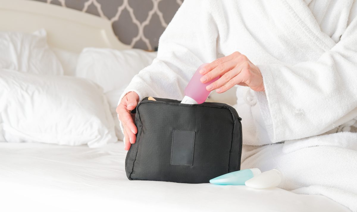 woman hands holding cosmetic travel kit on the bed. colorful cosmetic bottles and hygiene items for travel. Skincare Retail Kits for Salons.