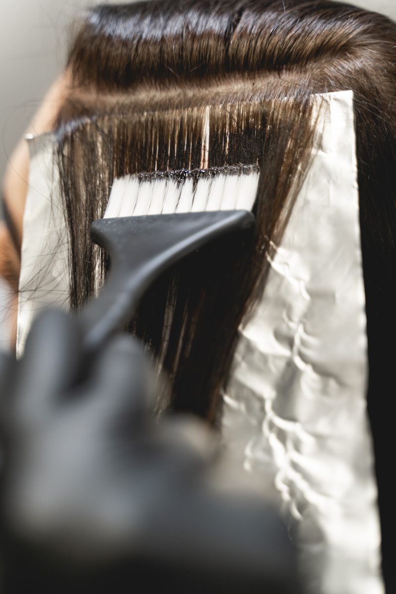 Close up of female person that using clean brush while coloring brunette hair in salon