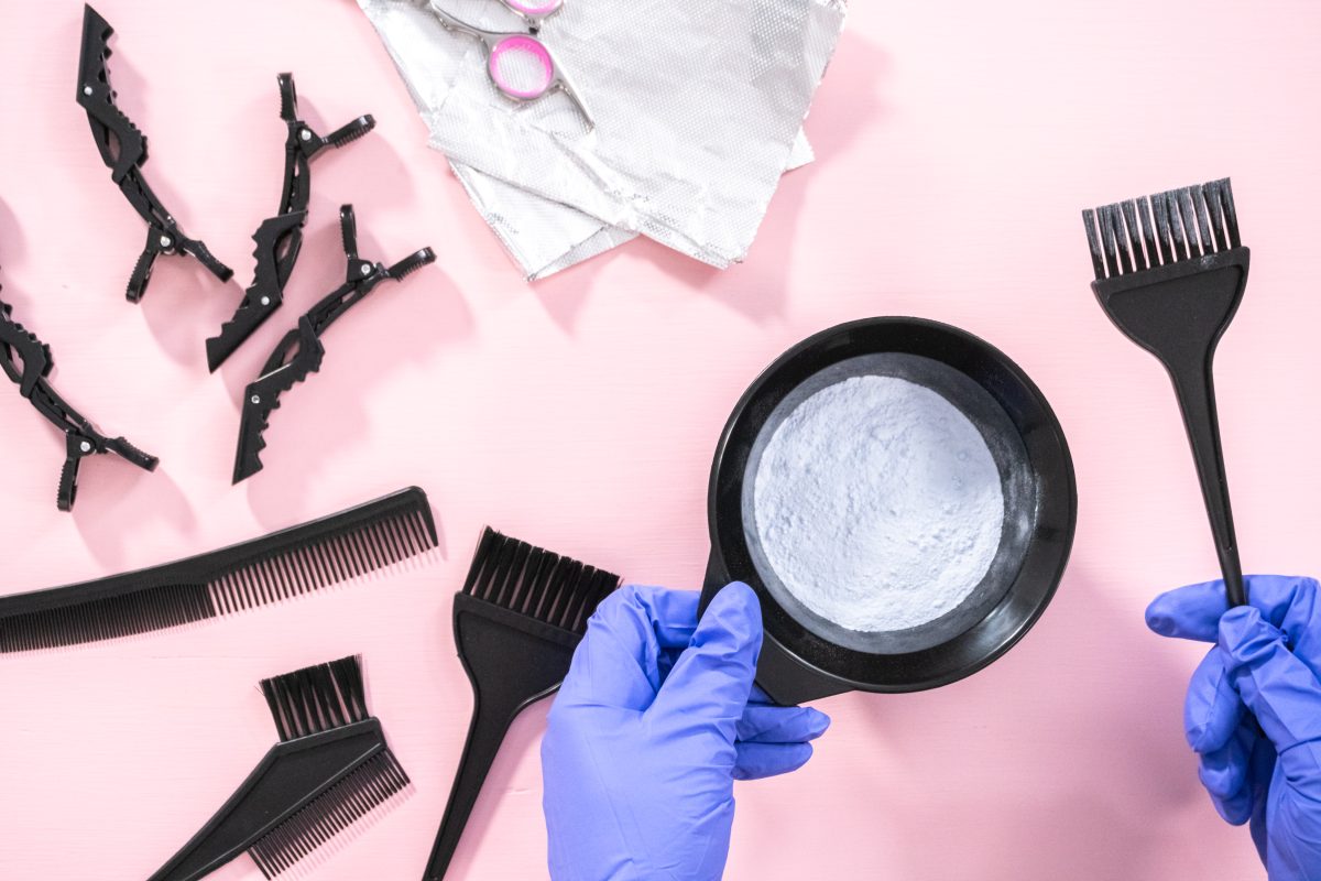 Flat lay. Hair color dye powder in a black plastic mixing bowl on a pink background.