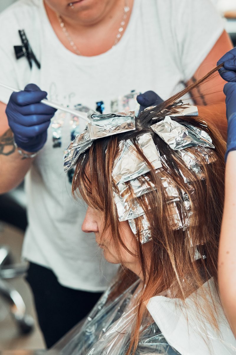 Best Hair Dye Products for Salons. Hairdresser styling dyeing combing womans hair. Young woman working as a hairdresser in hair salon. Real people, authentic situations