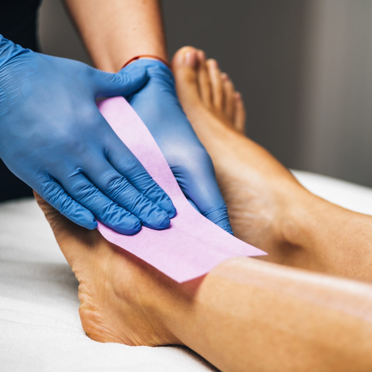 Soft wax. Hair removal. Waxing - Beautician Removing Unwanted Hair from Female Leg with Wax Strips in a Beauty Salon.