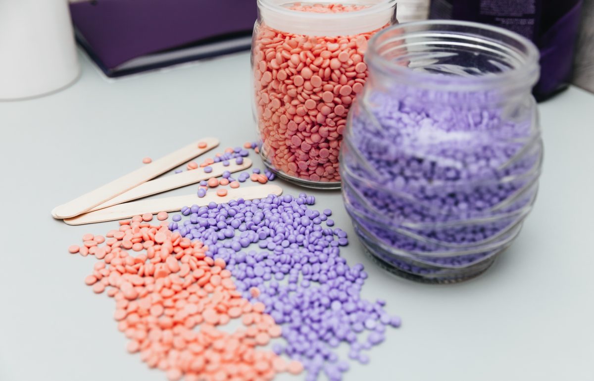 Close-up of lilac and pink wax granules scattered from a jar. Cosmetic procedure to remove unwanted hair from the body. depilation and epilation.