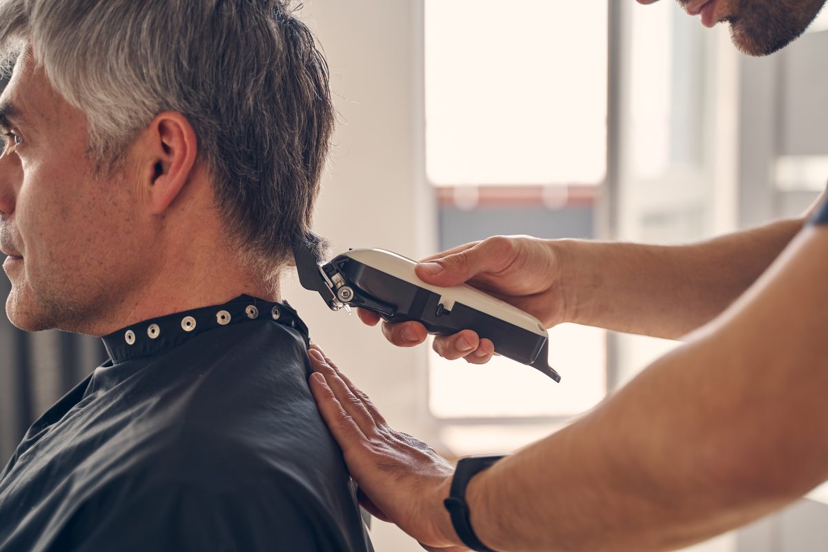 Cropped photo of a Caucasian man sitting quietly while another male changing his hairstyle with help of special hairdresser tools