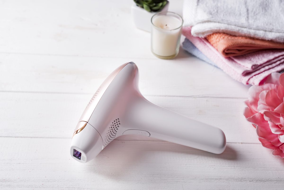 Modern laser epilator with bath accessories on white wooden background. Beauty and skin care concept