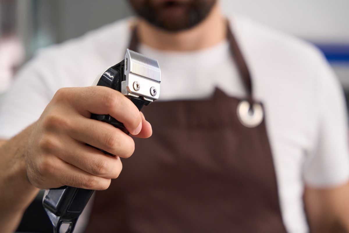 Cropped selective focus photo of barber in apron holding an electric hair trimmer