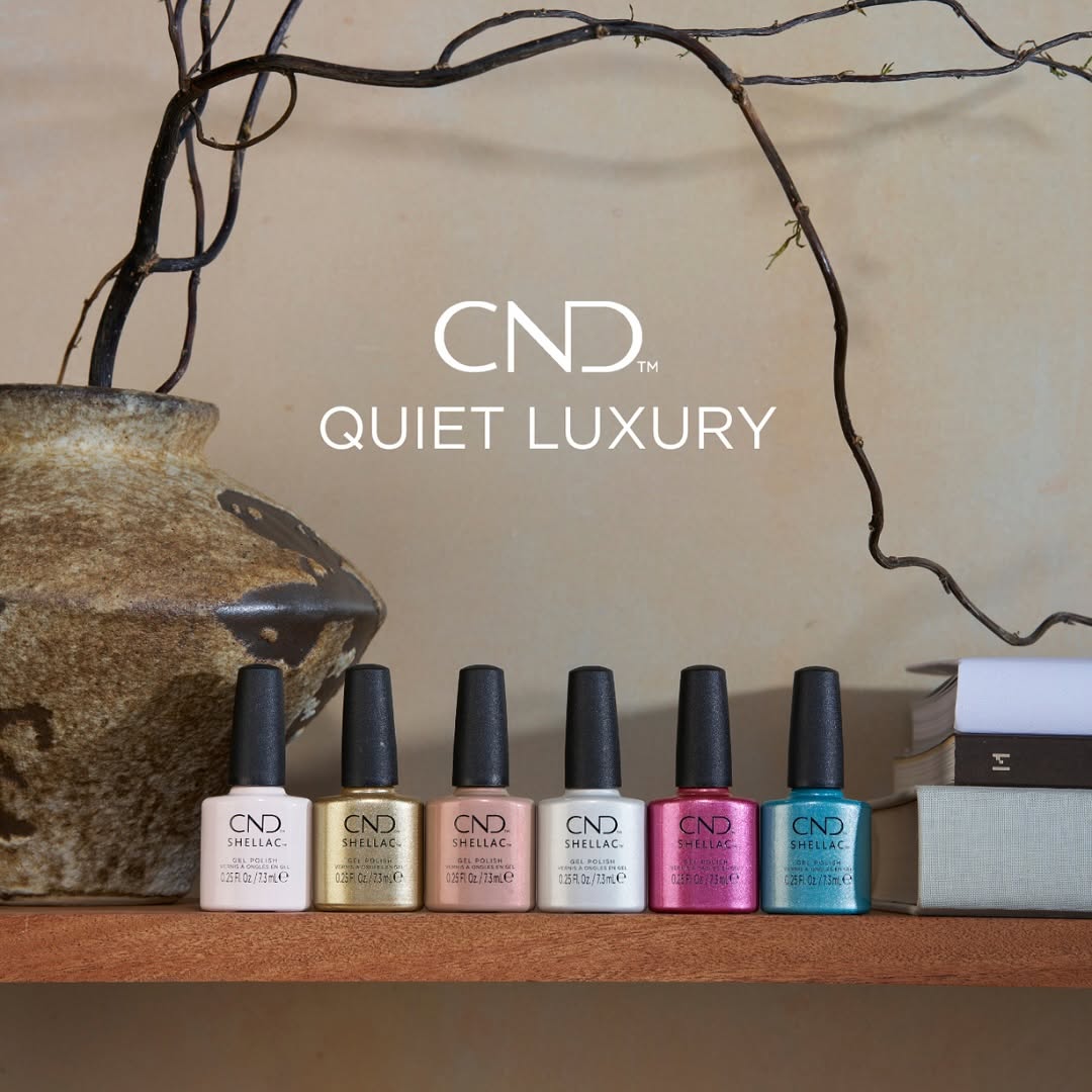 The full CND Shellac Quiet Luxury collection for Spring 2025, featuring six professional gel polish bottles on a wooden shelf: Of The Moment, Covetable, Pearlwind, Silk Thread, Sleeping Mask, and Gold Hardware.