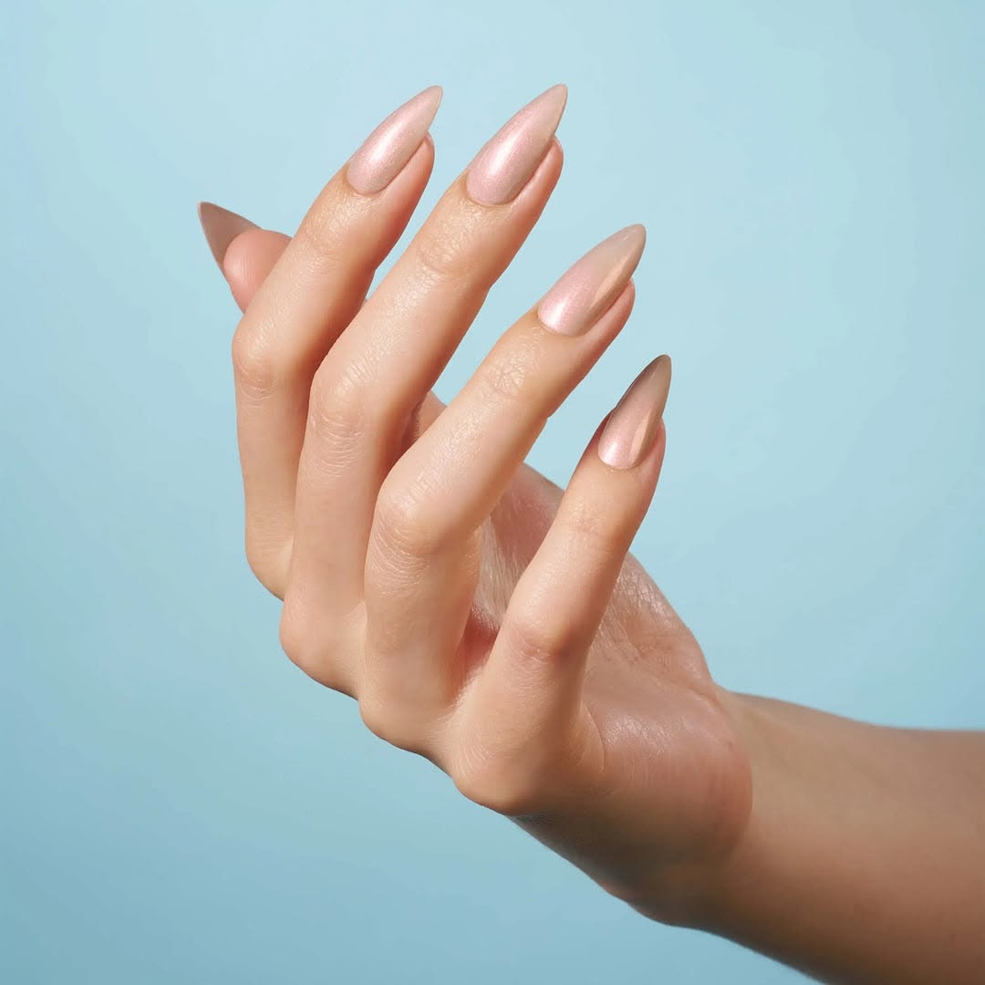 Hand with elegant, long stiletto nails coated in CND Shellac 'Covetable,' a beautiful shimmery pale rose gold from the new Quiet Luxury Spring 2025 collection.