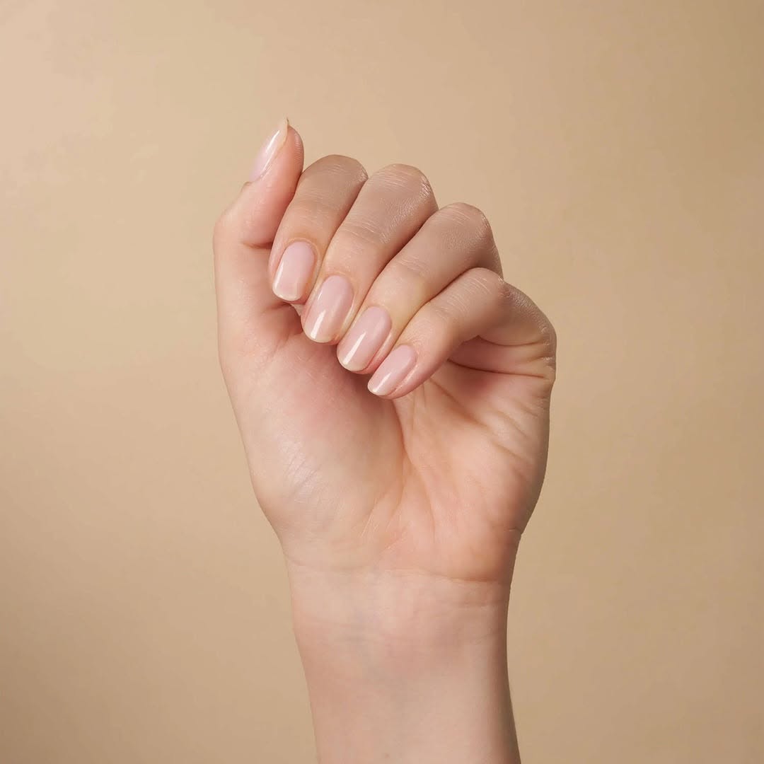 A hand with short, squoval-shaped nails painted with CND Shellac 'Pearlwind', a pearlescent white shimmer from the Quiet Luxury Spring 2025 collection, perfect for a chic and refined look.