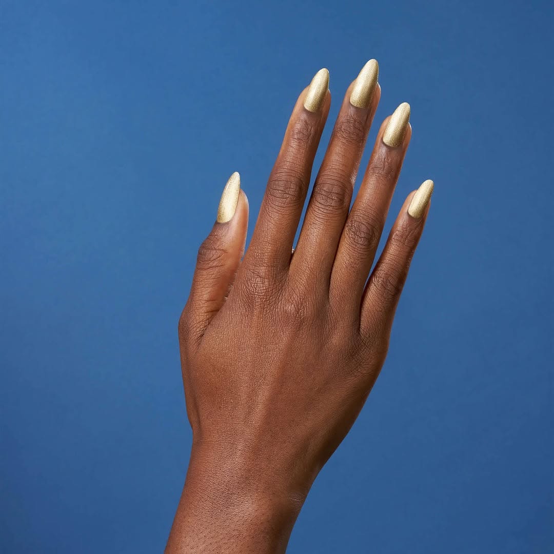 A hand with long, pointed nails in a radiant metallic gold, showcasing CND Shellac 'Gold Hardware' from the Quiet Luxury Spring 2025 collection, ideal for clients wanting a luxurious shimmer finish.