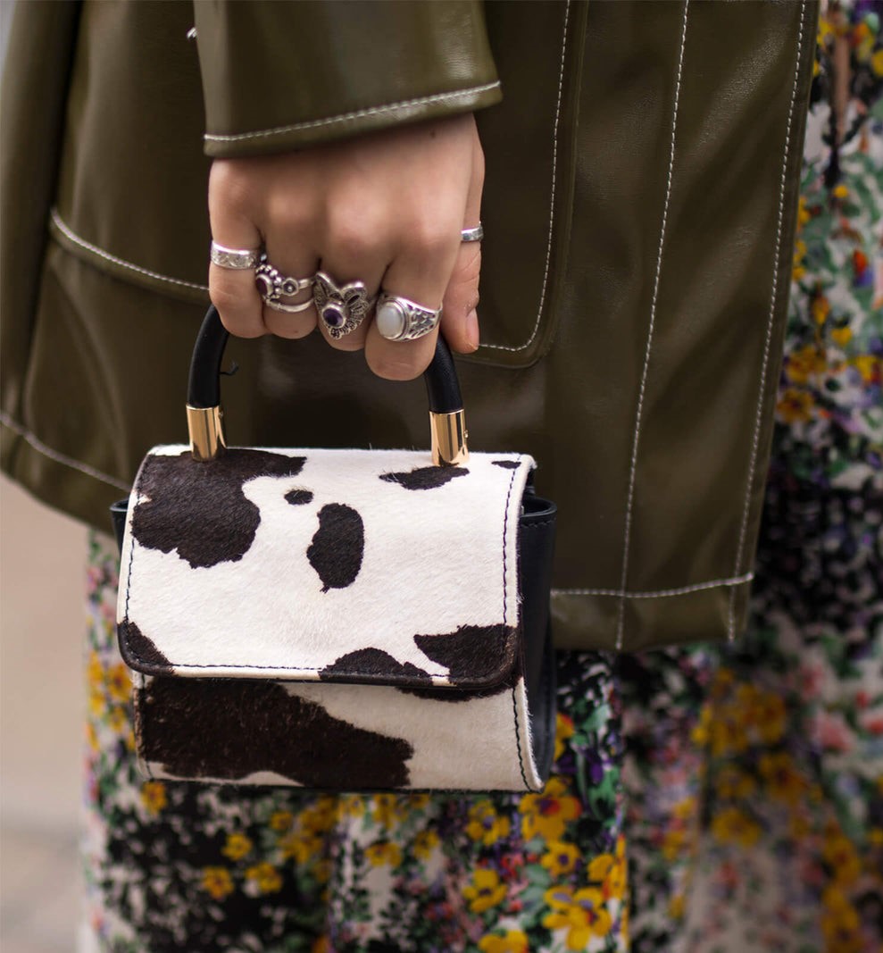 Close-up of a model showcasing eclectic fall styling with a cow-print handbag, silver statement rings, and floral pants—capturing the bold texture play and earthy elegance of CND Fall 2025 nail color trends. The mix of leather, gold accents, and botanical patterns reflects the season’s fusion of rustic charm and expressive individuality.