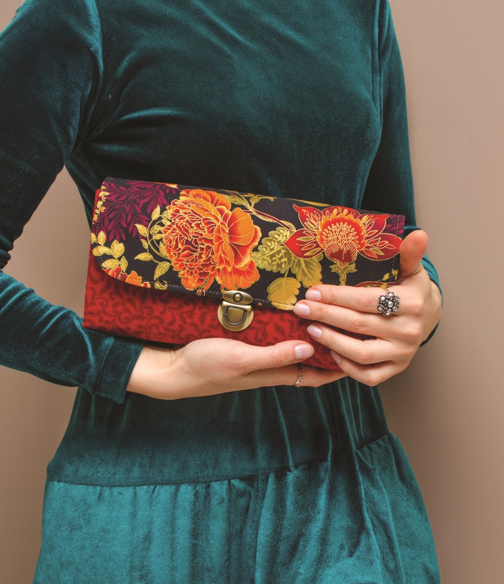 Model wearing a teal velvet dress holding a floral clutch, styled to reflect CND’s Fall 2025 nail color themes—Gothic Garden and Pretty Little Paisley. The rich textures and moody florals echo seasonal nail art trends, blending romantic botanicals with autumn fashion.