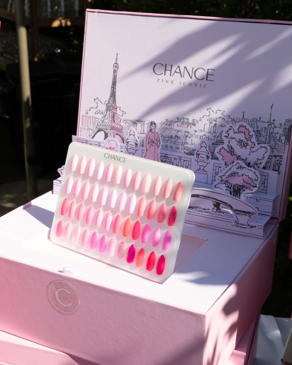Outdoor display of the Chance "Pink Iconic" 48-color swatch board held in front of the open collection box. The board showcases the full spectrum of pinks—from milky nude pastels to deep fuchsias and bright magentas—essential for bridal and trendy pink nail art. The collection box features a Parisian-themed Eiffel Tower illustration. Chance Creation Collections