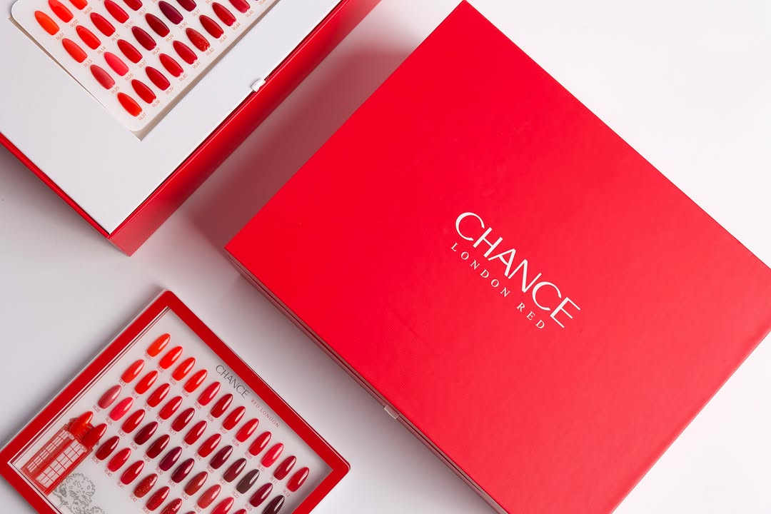 High-angle flat lay showing the elegant, closed Chance "London Red" gel polish collection box alongside two separate swatch displays. The large red box features white text, "CHANCE LONDON RED." The visible swatch boards demonstrate the kit's full 48-color range, an essential full-line red gel polish set for professionals. Chance Creation Collections