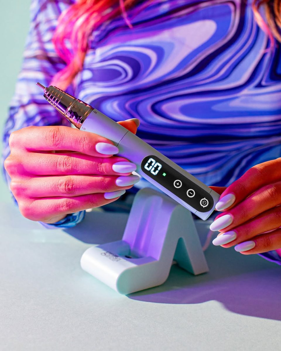 Aqua Marine Gelish Go File Wireless E-File being placed into a white magnetic charging dock by a person with lavender manicured nails. The sleek cordless nail drill features a digital display reading "00" and four touch-sensitive buttons. Set against a vibrant blue and purple background, the image highlights the device’s stylish design, ergonomic grip, and salon-grade performance.
