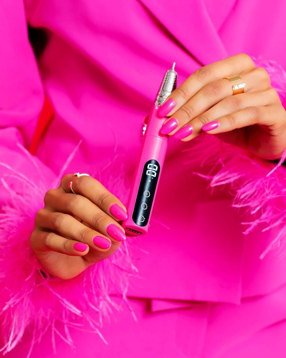 Vivid Magenta Gelish Go File Wireless® E-File held by a faceless woman in a matching pink outfit with manicured nails. The cordless nail drill features a digital display showing 35, three control buttons, and a sleek ergonomic design. Includes magnetic charging dock. Ideal for professional nail technicians seeking a stylish, high-performance, portable e-file.