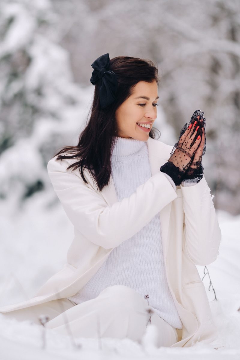 Portrait of a stylish woman in a white suit with elegant gloves sitting in nature in winter. Winter 2025 colors. Winter 2025 nail polish shades. Holiday nails. Holiday nail trends