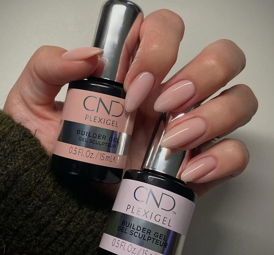 A professional close-up of almond-shaped nails with a nude gel manicure, featuring bottles of CND Plexigel Builder Gel (0.5 Fl. Oz / 15 mL). The image highlights a smooth, glossy finish on a natural-toned extension, showcasing a collaborative design by CND X @OPALTOUCHNAILS. CND PLEXIGEL Application