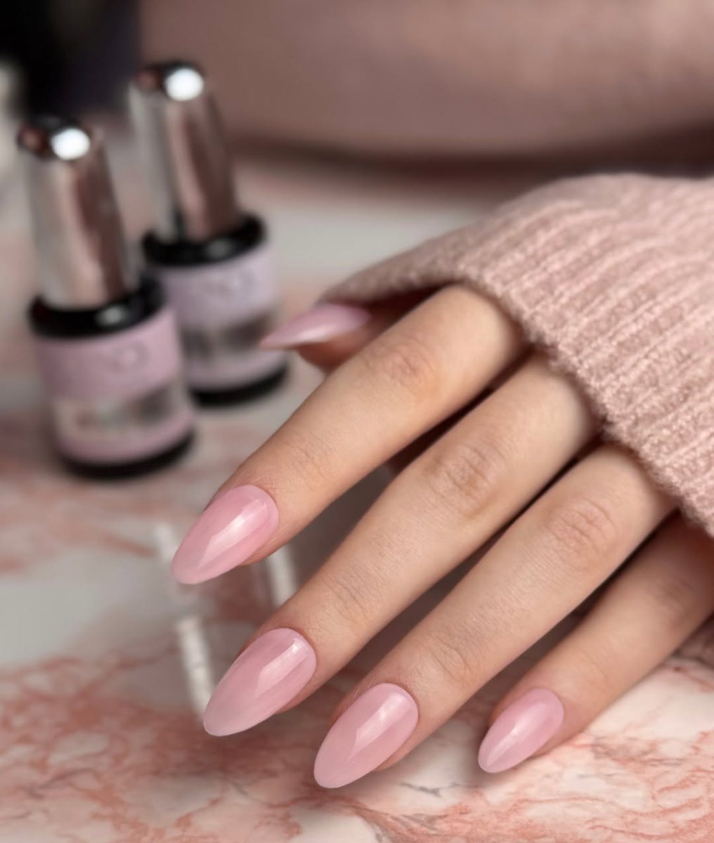 Professional manicure featuring CND Plexigel Builder Gel in a neutral nude shade. Close-up of almond-shaped nails with a glossy finish, held next to two CND Plexigel bottles.