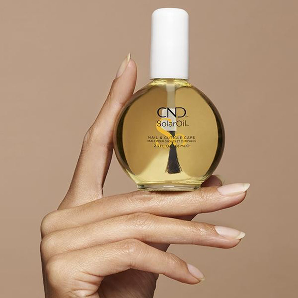 Hand holding the larger, round bottle of CND SolarOil Nail & Cuticle Care (2.3 fl oz / 68 mL), illustrating the generous size option for frequent and deep nail conditioning.