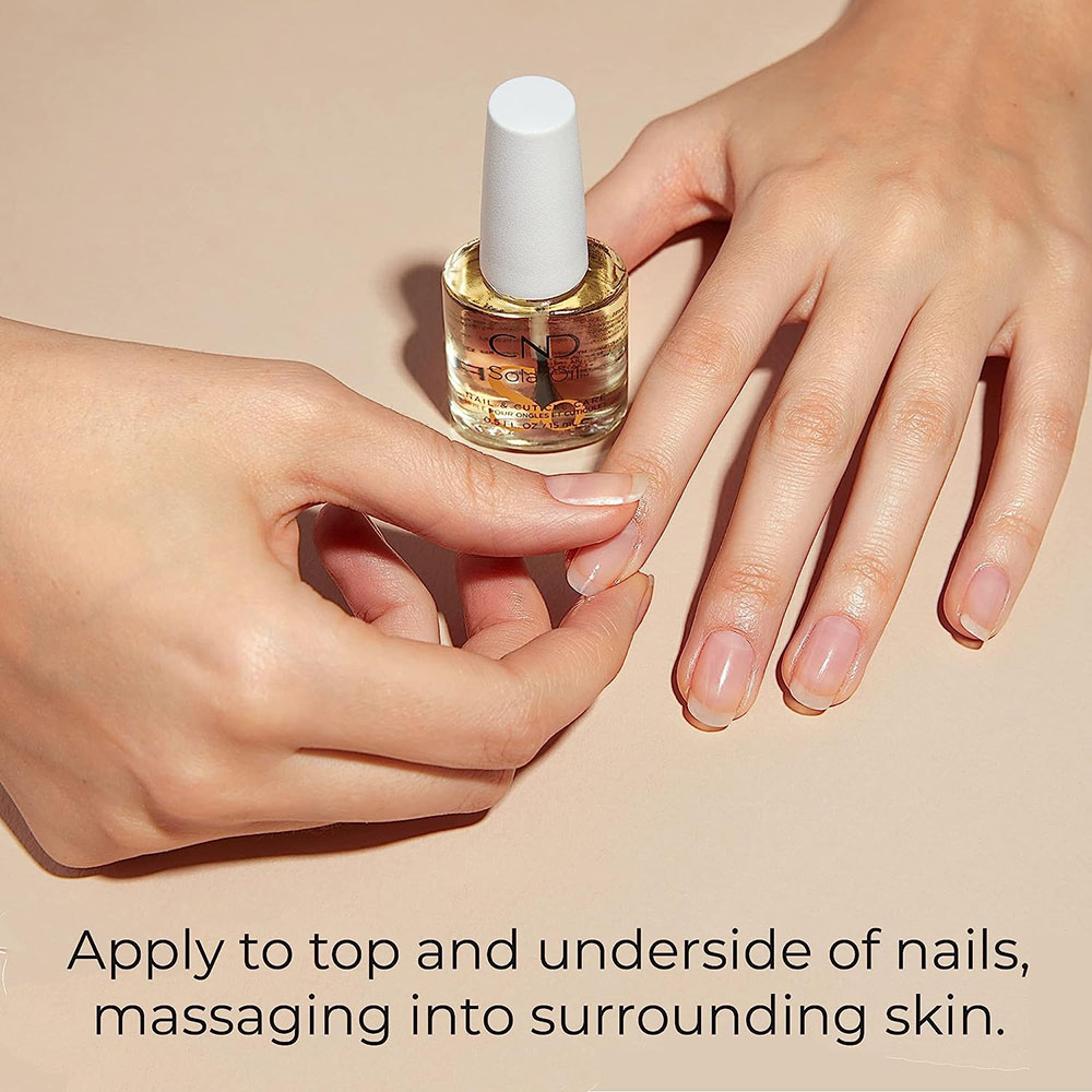 Close-up of a person applying CND SolarOil to their bare nail and cuticle area, demonstrating the recommended application technique to the top and underside of the nail for maximum moisture and strength.