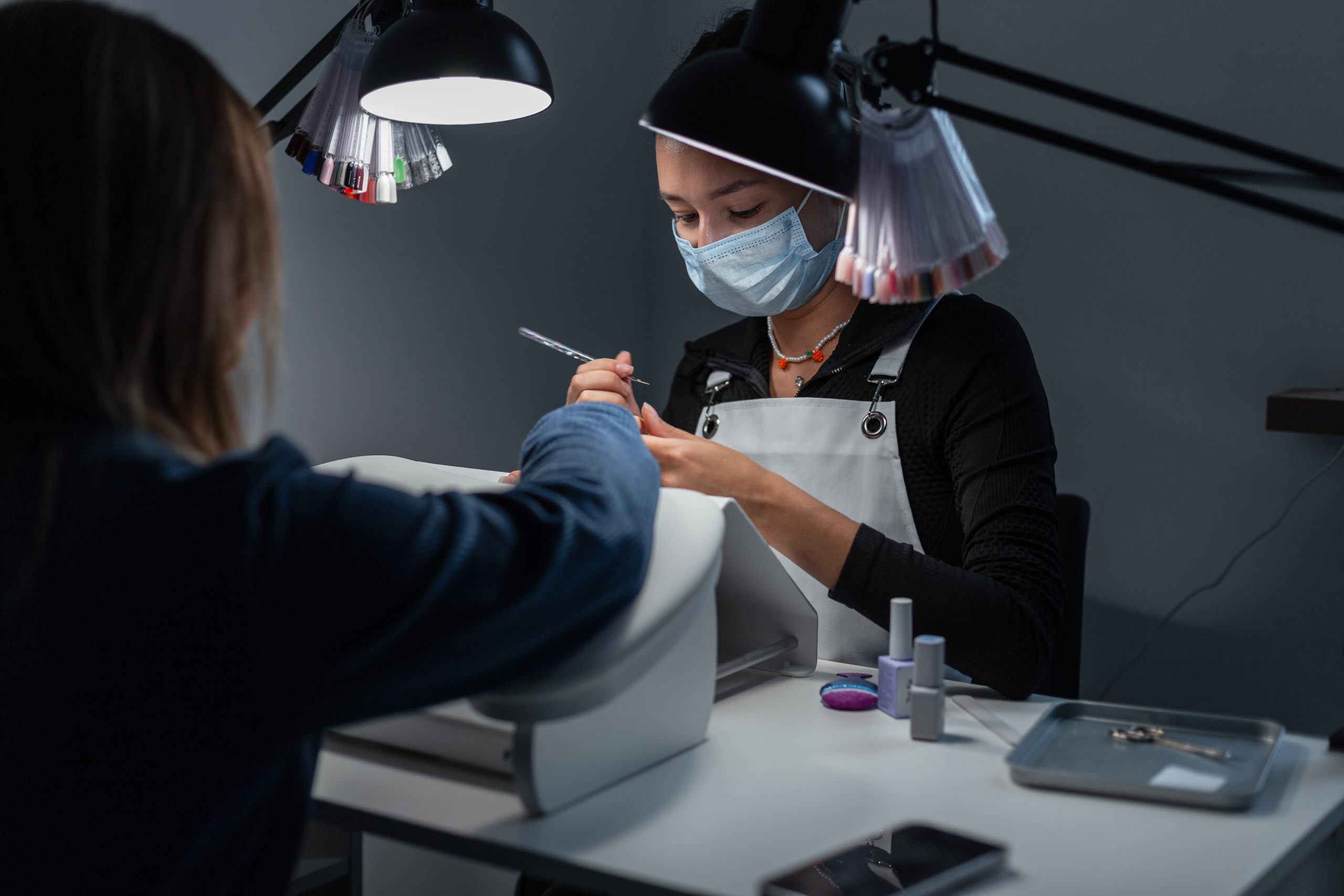 Pricing Polygel Services. Beautiful professional woman sits and does manicure under lamps. Girl does hand and nail care in beauty studio