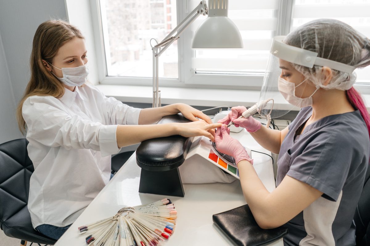 Pricing Polygel Services in Canada. Young woman getting manicure in beauty salon. Manicurist remove old manicure. Protective masks.