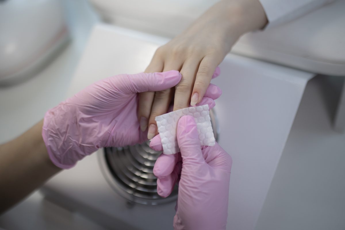 Professional nail technician performing safe gel removal and prep by cleaning the nail plate with a lint-free wipe and sanitizer.