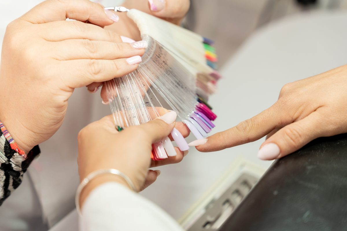 Beautician presenting a vibrant nail polish color palette to a customer, who is selecting her perfect shade in a stylish beauty salon, surrounded by an array of trendy options