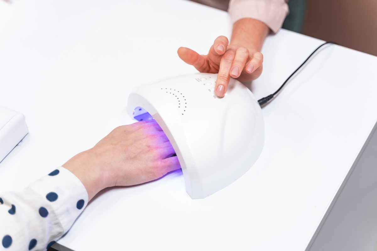 Modern technology. Young woman drying her nails in ultraviolet lamp while preparing for date. Beauty concept