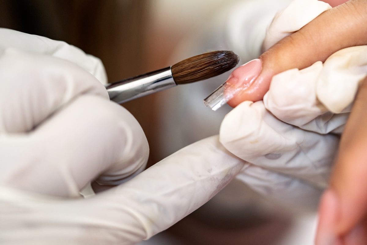 Professional manicurist applying acrylic on client's fingernail using a brush and plastic form. 