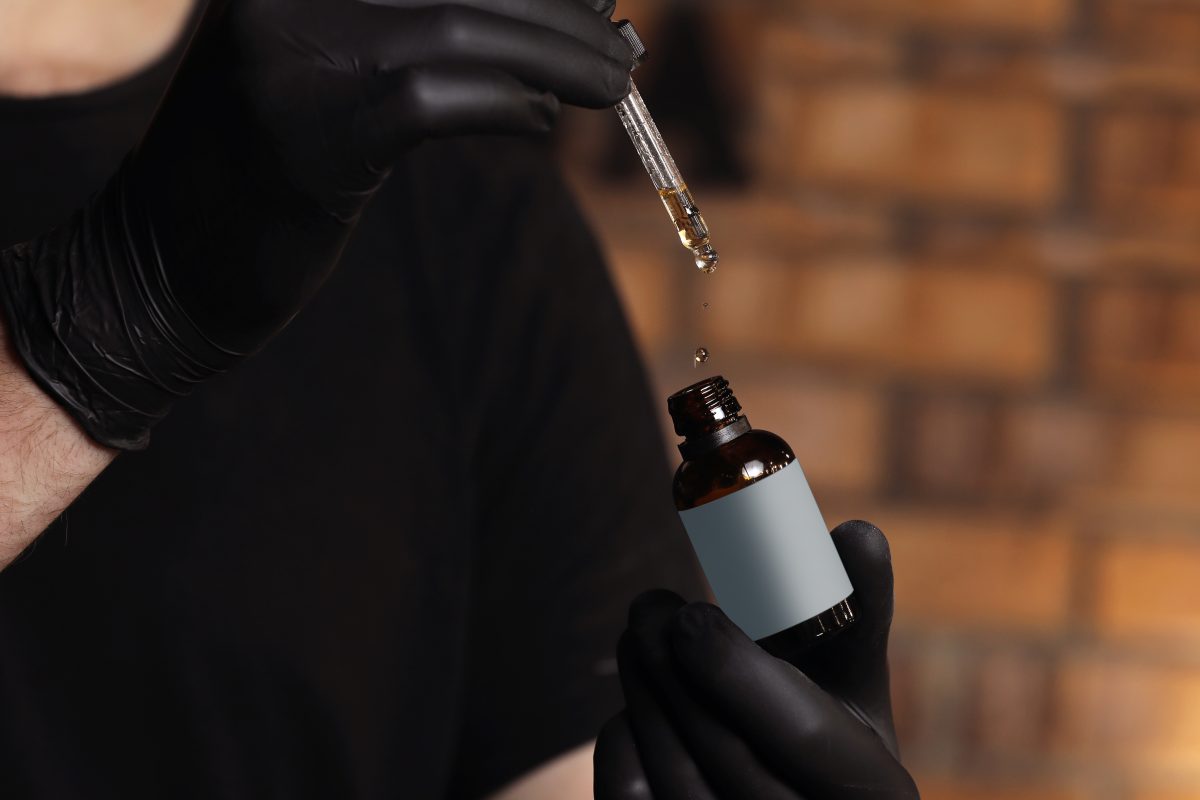 Dropper glass Bottle Mock-Up. Oily drop falls from cosmetic pipette on dark background. Opened vaping e-liquid dropper bottle with drop on pipette. selective focus. place for text. Hair serum. Hair treatment.