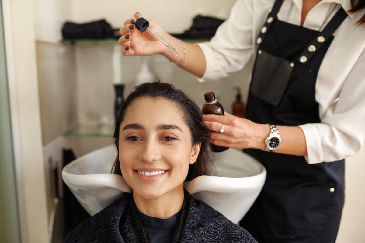 Hairdresser works with woman's hair, hairdressing salon. Stylist and client in hair salon. Beauty business, professional service. Hair serum. Hair treatment. Hair oil.