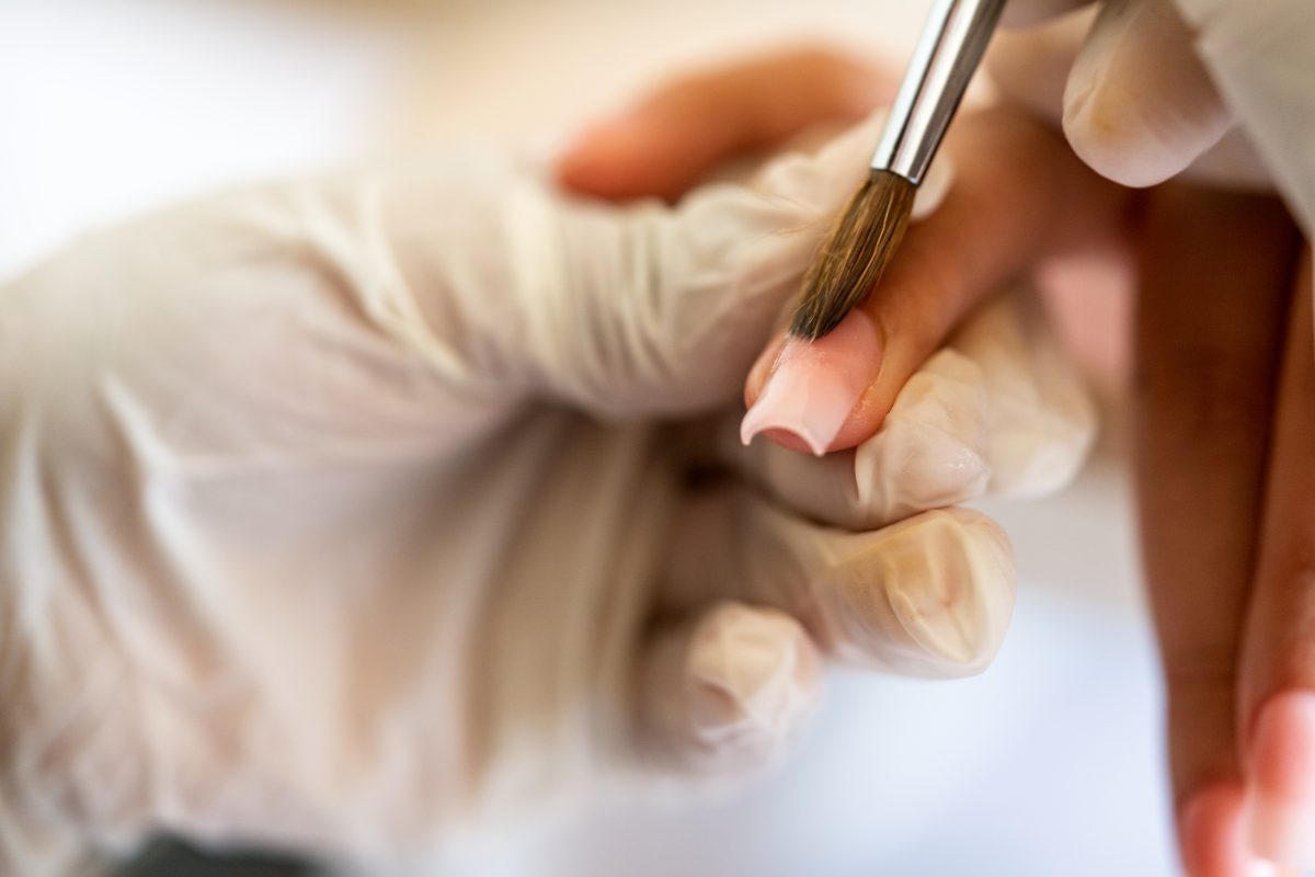 Close-up of a nail technician using a professional brush to apply acrylic polymer for seamless acrylic fills.
