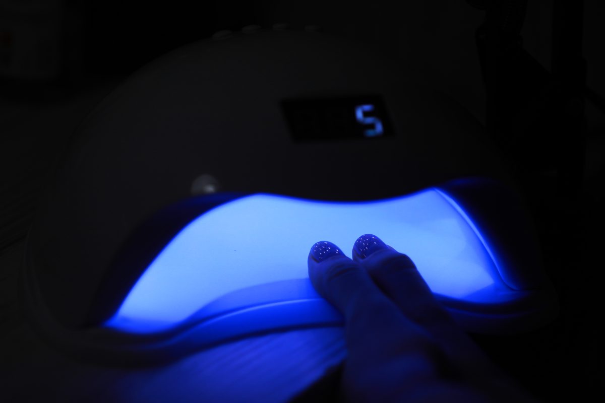Closeup view of female hands with gel polish manicure. Woman puts hand into led uv lamp for curing top cover of nail polish. UV lamp, LED Nail.