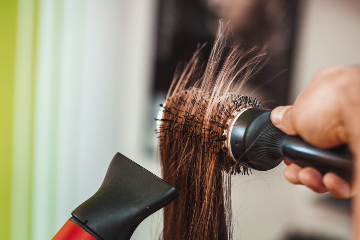 Close-up of a hairdressers hands drying brown hair with round brush of a female customer.