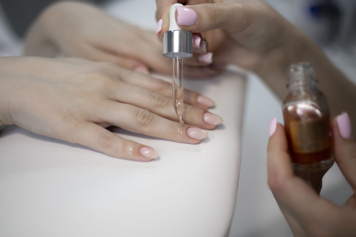 Professional nail technician applying nourishing cuticle oil after completing acrylic fills to hydrate the skin.