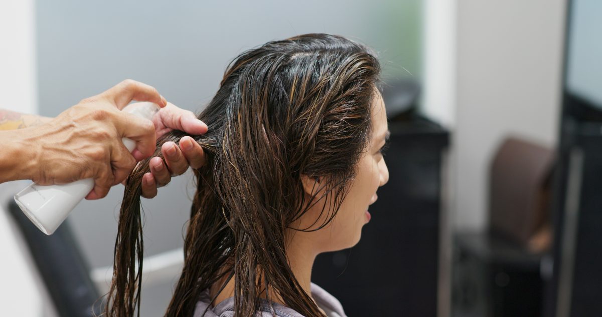 Heat Damage Recovery treatment with a professional hairstylist straightening a woman’s hair using a flat iron in a salon.