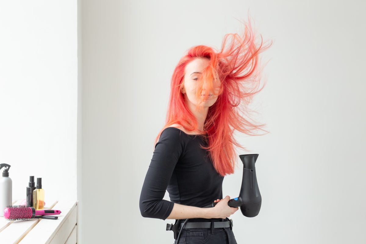 Hairdresser and beauty salon concept featuring a young hairstylist using a hair dryer during a Heat Damage Recovery treatment on a white background.