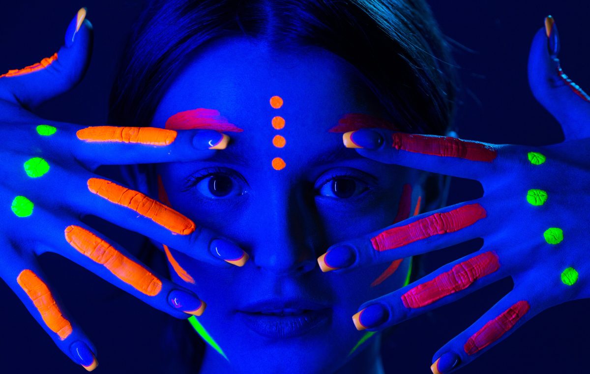 Portrait of beautiful girl with ultraviolet paint on her face. Girl with neon make-up in color light.