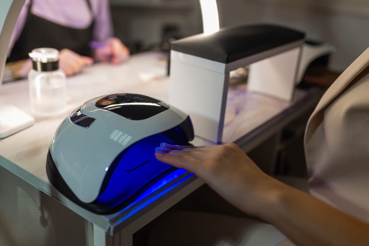 Close up of female hand curing gel nail polish under UV LED lamp in beauty salon. Professional manicure process, nail drying, cosmetic treatment, hygiene and nail care concept. Best professional LED nail lamp