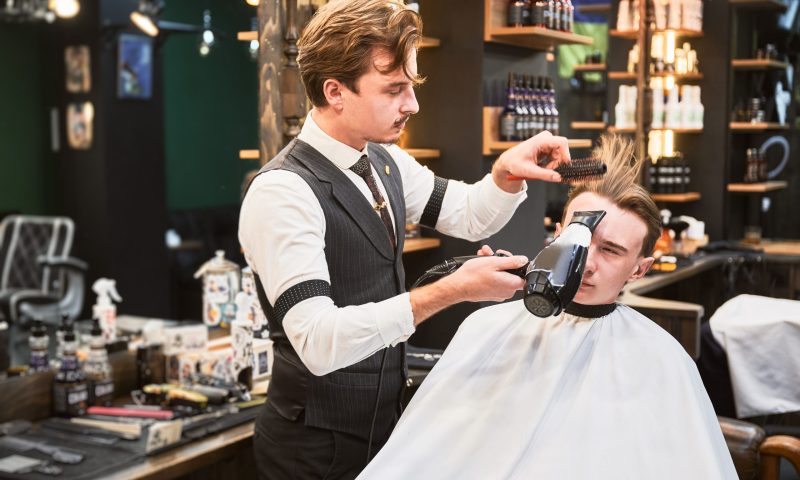 Barber styling a client's hair with a dryer and brush.